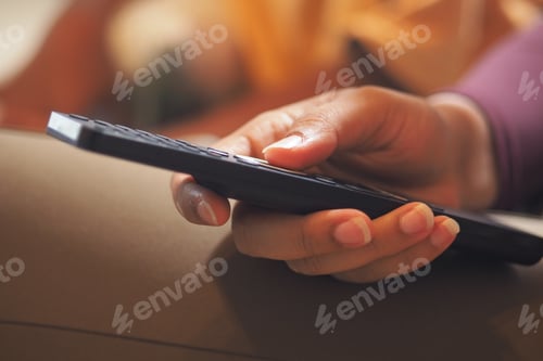 Preview: Hand holding a remote control while watching TV