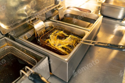 Preview: in professional kitchen frying French fries in oil in a deep fryer