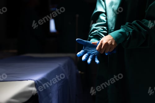 Preview: Midsection of surgeon putting on glove in dark operating theatre, with copy space