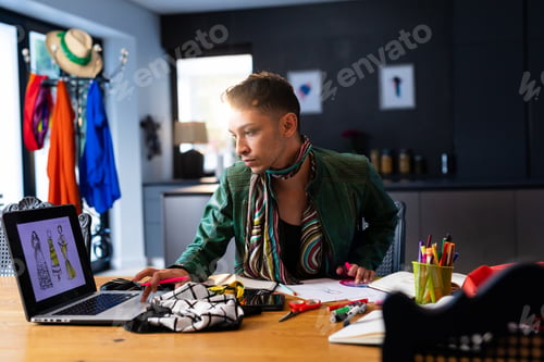 Preview: Biracial transgender fashion designer sitting at desk and using laptop