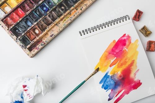 Preview: top view of watercolor paints and paintbrush at designer workplace