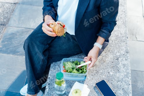 Preview: Top view close up business woman eating sandwich and fresh salad on lunch break sitting on bench