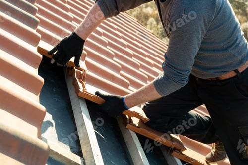 Preview: Closeup of worker hands installing yellow ceramic roofing tiles