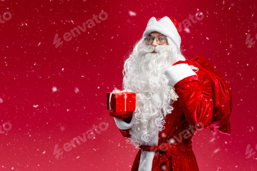 Preview: Portrait of Saint Nicholas holding gift box and bag looking at camera isolated on red background