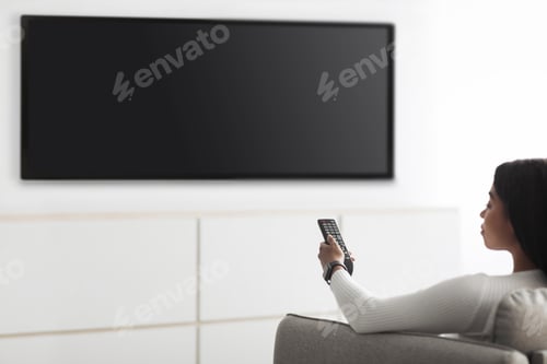 Preview: Black lady watching television, turning on plasma flatscreen TV-set, pointing remote control at