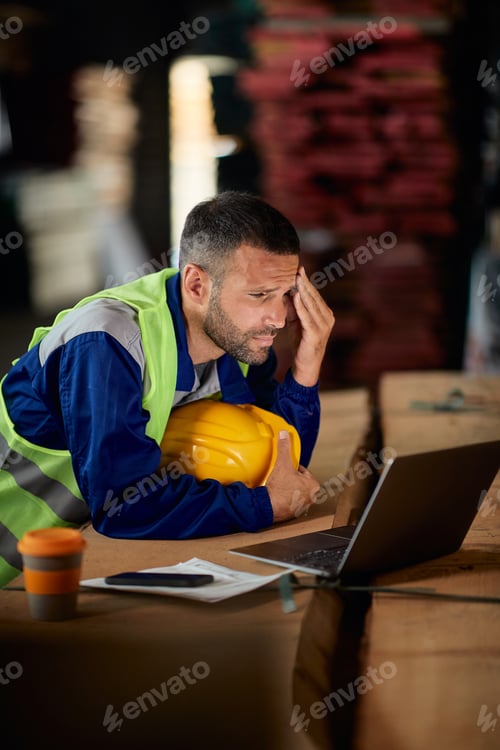 Preview: Worried warehouse worker reading problematic e-mail on laptop.