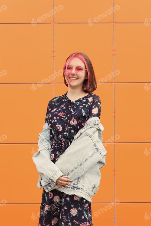 Preview: Young girl with pink glasses on the background of an orange wall