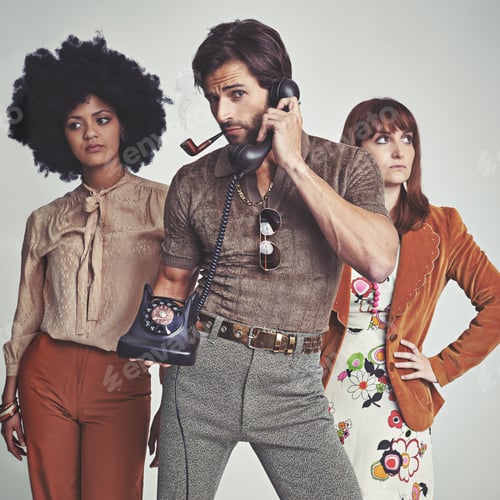 Preview: Two attractive young hippies standing behind a handsome man using a retro telephone