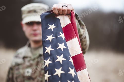 Preview: Selective focus shot of an American soldier holding the American flag close to the camera