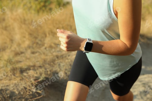 Preview: Woman wearing modern smart watch during training outdoors, closeup
