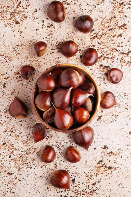 Preview: Wooden bowl filled with chestnuts on beige stone kitchen table, perfect for seasonal food themes.