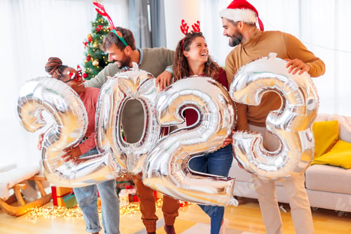 Preview: Friends holding big balloons shaped as numbers 2023 while celebrating New Year at home
