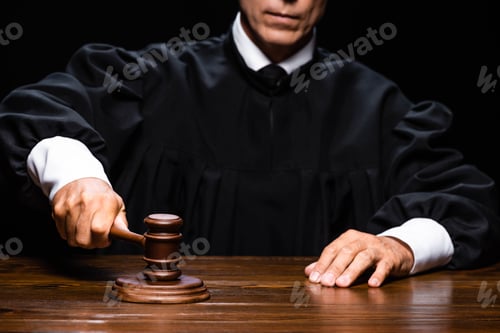 Preview: cropped view of judge in judicial robe sitting at table and hitting with gavel isolated on black