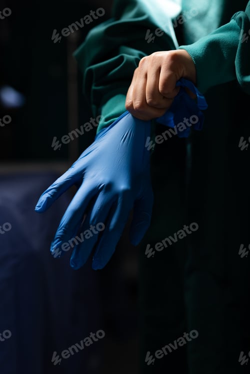 Preview: Vertical of midsection of surgeon putting on glove in dark operating theatre, with copy space