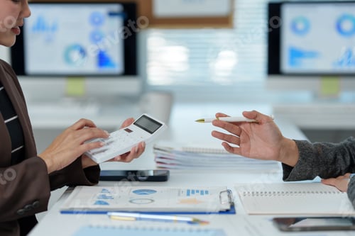 Preview: Two business professionals collaborate in an office, examining financial reports and using a calcula