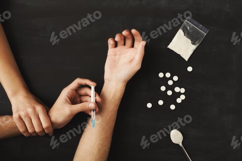 Preview: Drug addict hands holding syringe for injection on dark table