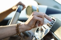 Preview: Hand of man with bracelets wipes panel vent with white napkin holding steering wheel driving car