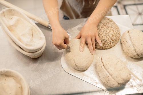 Preview: women's hands make an incision on a round dough before baking bread