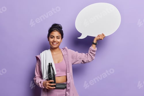 Preview: Positive sporty woman holds communication bubble and bottle of water smiles gladfully poses with
