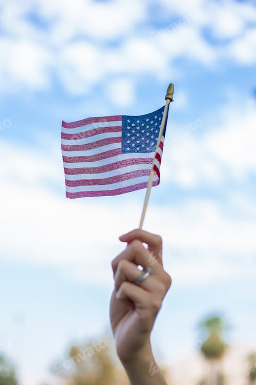 Preview: Vertical shot of a hand waving an American flag outdoors