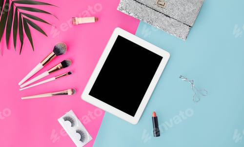 Preview: Girlish composition with digital tablet and various makeup products on blue and pink background, top