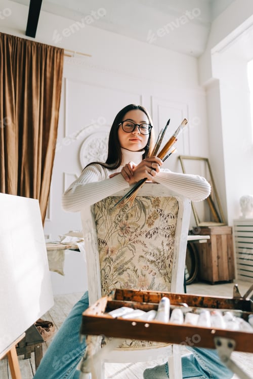 Preview: Female Artist Sitting Holding Brushes in Bright Studio