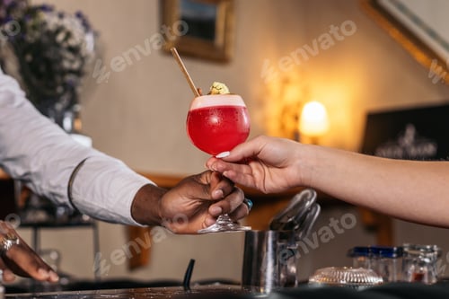 Visualização: Recorte de um barman preto oferecendo um coquetel servido em um copo em um bar de coquetéis tradicional