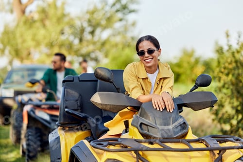 Preview: Portrait of a smiling woman driving a rental quad bike, with sunglasses on.