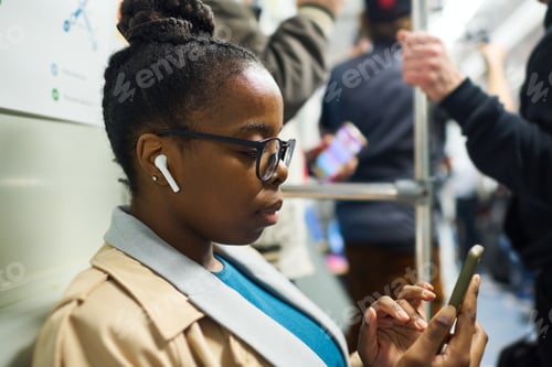 Preview: Young serious African American businesswoman in earphones using mobile phone