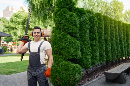 Preview: Muscular gardener holding electric hedge trimmer outdoors