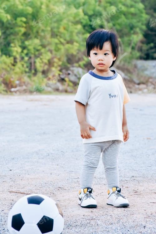 Preview: Asian kid playing soccer or football in the park.
