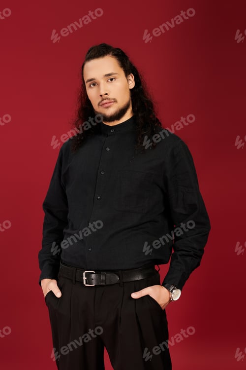 Preview: Handsome young bearded man in stylish outfit poses confidently against a vibrant red backdrop