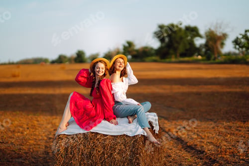 Preview: Two smiling young woman resting near haystack. Fashion concept. Nature, vacation, relax, lifestyle.