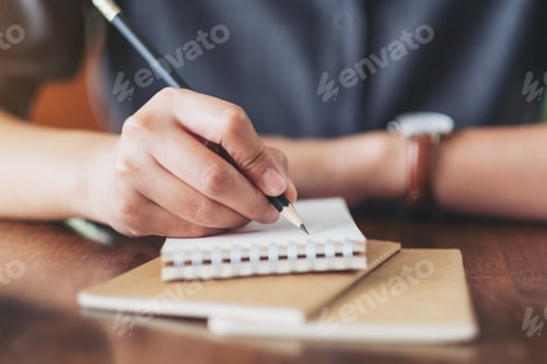 Preview: Closeup image of a woman's hand writing on blank notebook on wooden table