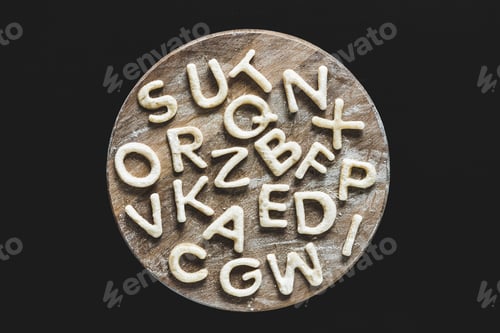 Preview: Top view of edible letters from dough on wooden cutting board, baking cookies concept