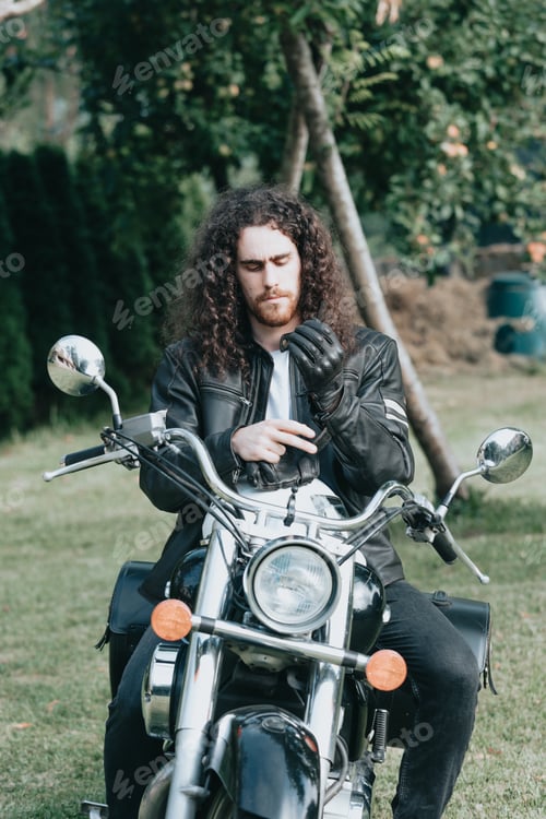 Preview: Portrait of a young long hair man, an old biker in a leather jacket on a retro bike