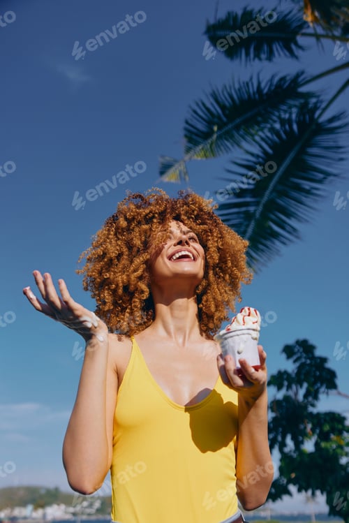 Preview: Happy woman enjoying ice cream outdoors with palm trees in the background under a clear blue sky