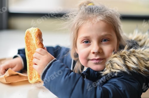 Preview: girl in winter jacket takes small, careful bites of puff pastry bun.