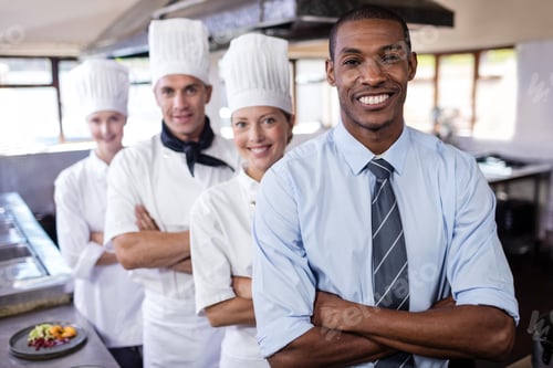 Preview: Group of chefs and manager standing with arms crossed in kitchen at hotel