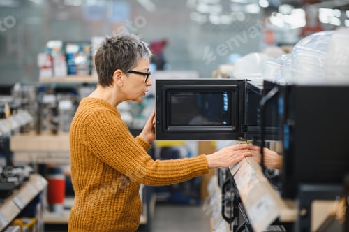 Preview: Senior woman opening new microwave in appliance store