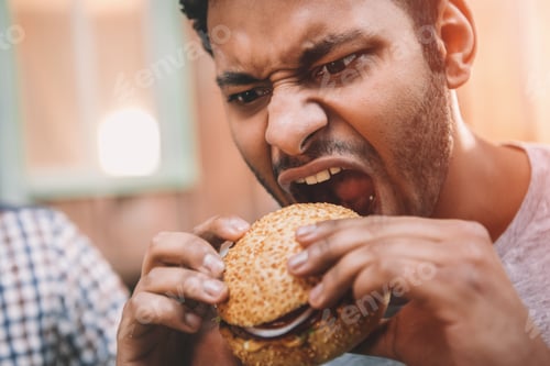 Preview: Close-up view of hungry young man biting gourmet homemade hamburger