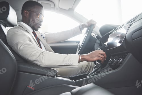 Preview: Stylish black businessman sitting behind the wheel of new luxury car. Rich african american man