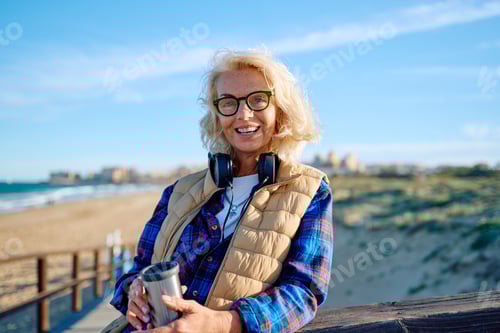 Preview: Happy woman enjoying morning coffee on beach boardwalk in sunny weather