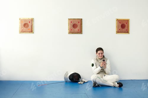 Preview: Female fencer sitting on floor using cell phone