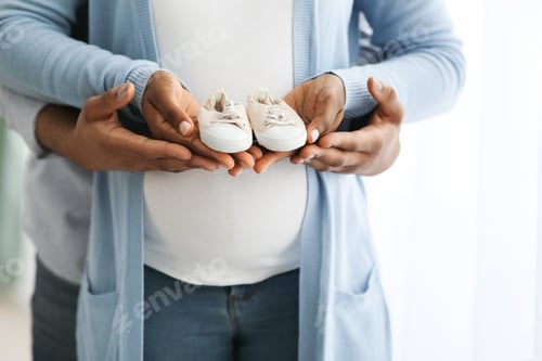 Preview: Cropped of pregnant african american family holding small baby shoes