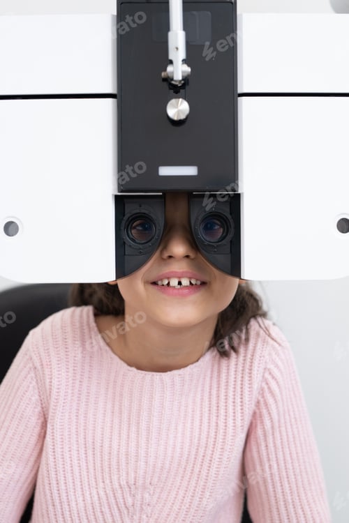 Preview: Face of happy cute schoolgirl sitting in front of ophthalmological equipment