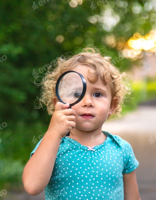 Preview: A child looks through a magnifying glass in nature. Selective focus.