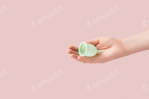Preview: Menstrual cup in a female hand against a pink background