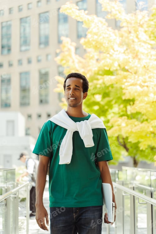 Preview: Portrait of smiling African American man holding books, standing in park, looking at camera