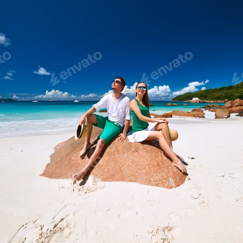 Preview: Couple In Green Sitting On A Rock At Tropical Seychelles Beach